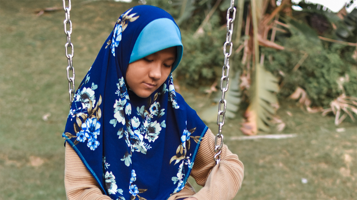 A youth sitting on a swing with their face looking down.