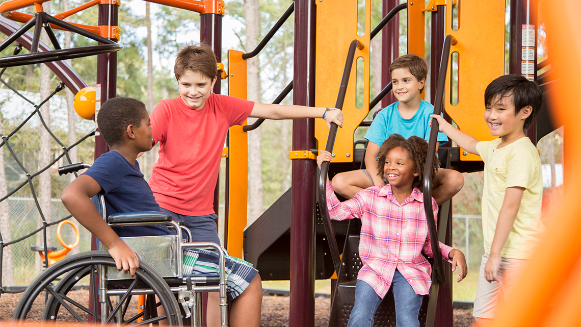 Children chatting and having fun on a playground. One child uses a wheelchair.