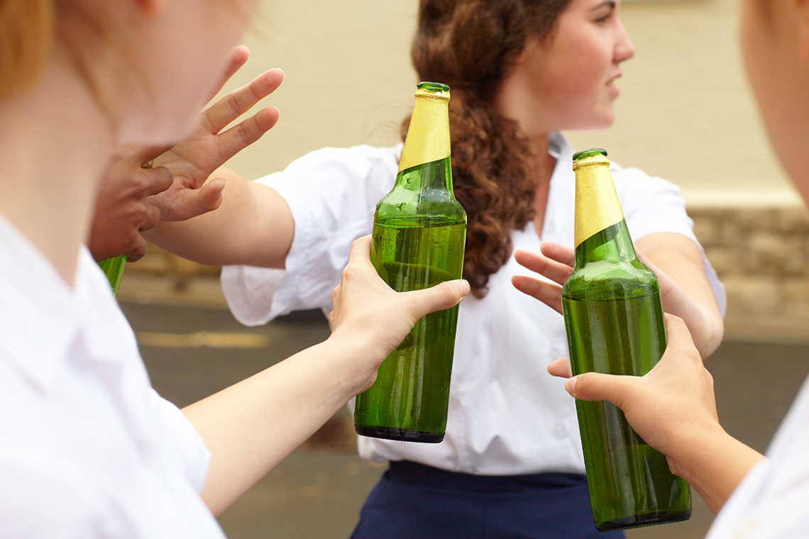 A student is refusing alcohol from their peers by putting their hand up in a ‘stop’ position. Alcohol is being offered to them.