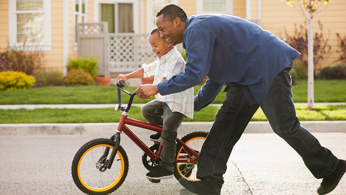 An adult is helping a child balance on a bike.