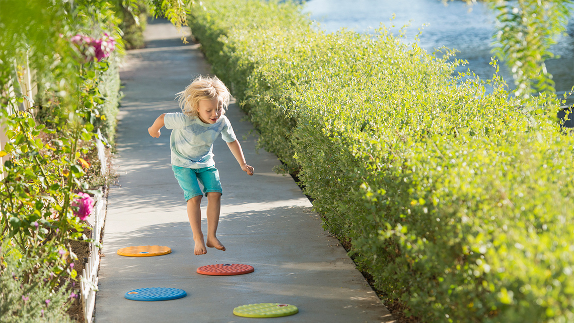 A child is keeping balance as they are stepping on different colourful steps on the ground.