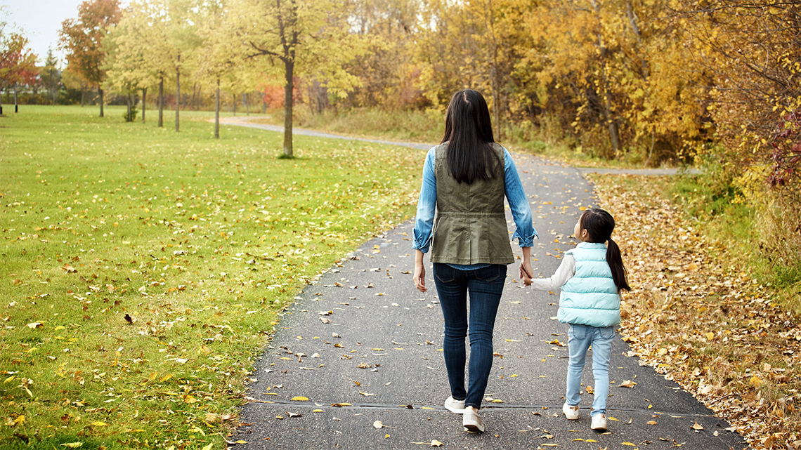 An adult and a child walking in the park.