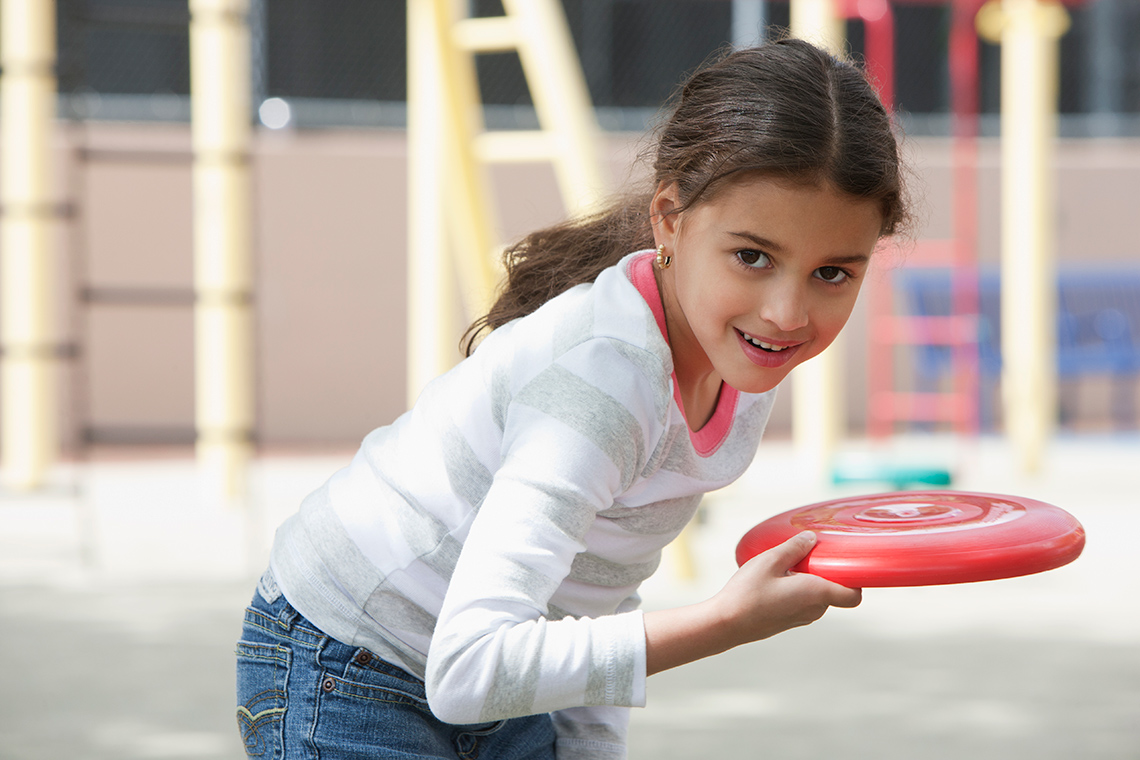 A child is getting ready to throw a frisbee. Their back and arm are bent before the frisbee is sent.