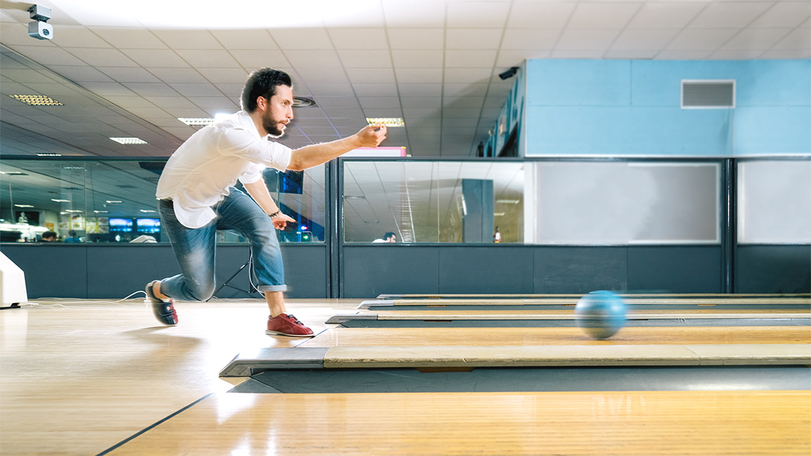 An adult is sending a bowling ball down the aisle.