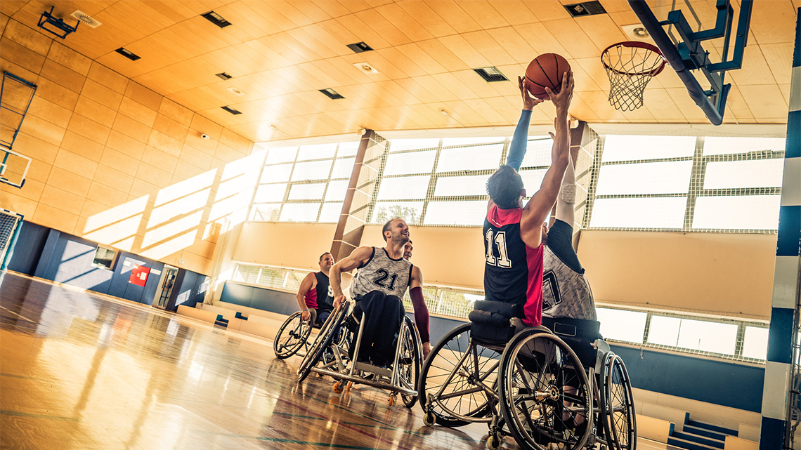 A basketball player, in a wheelchair, is sending a ball to the net.