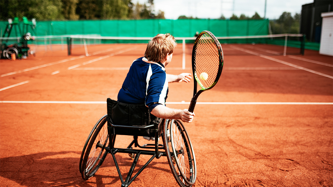 A tennis player, in a wheelchair, is sending the ball to their opponent.