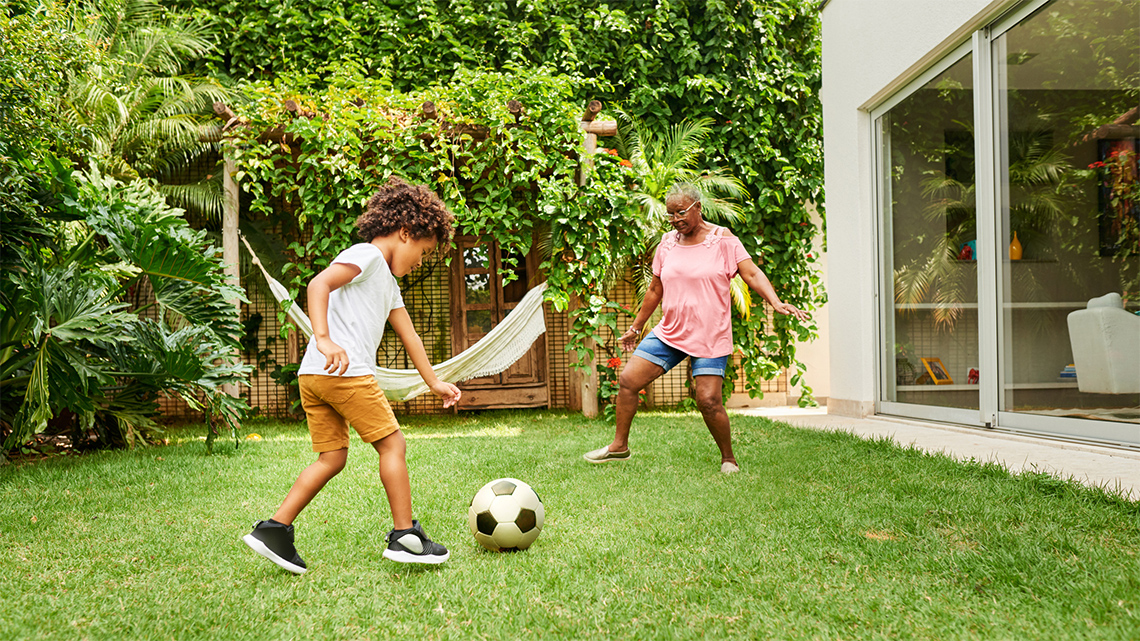 An adult and a child playing with a soccer ball in a backyard.