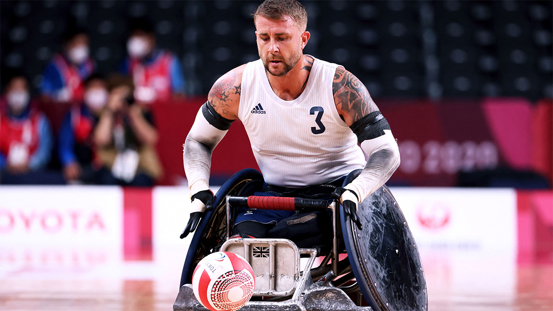 An adult, in a wheelchair, is receiving the ball in a rugby game.