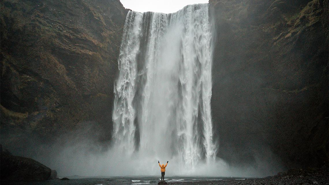 A waterfall pours over the edge of a tall cliff into a river.