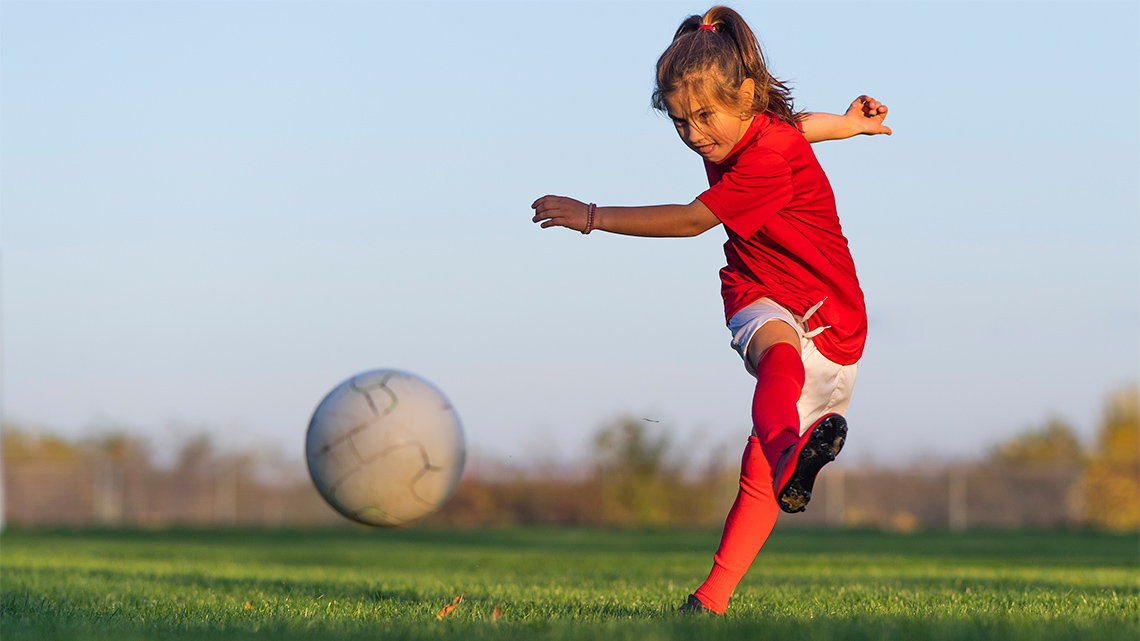A person kicking a soccer ball into a net.