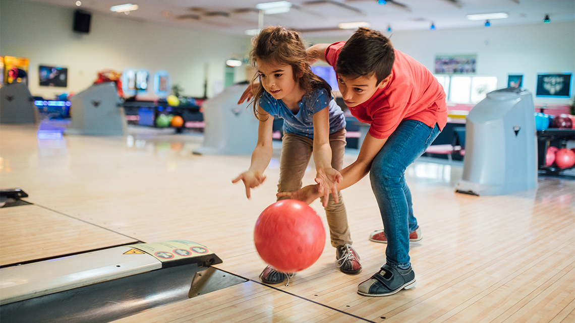 Two children in a bowling alley rolling a bowling ball down the lane.