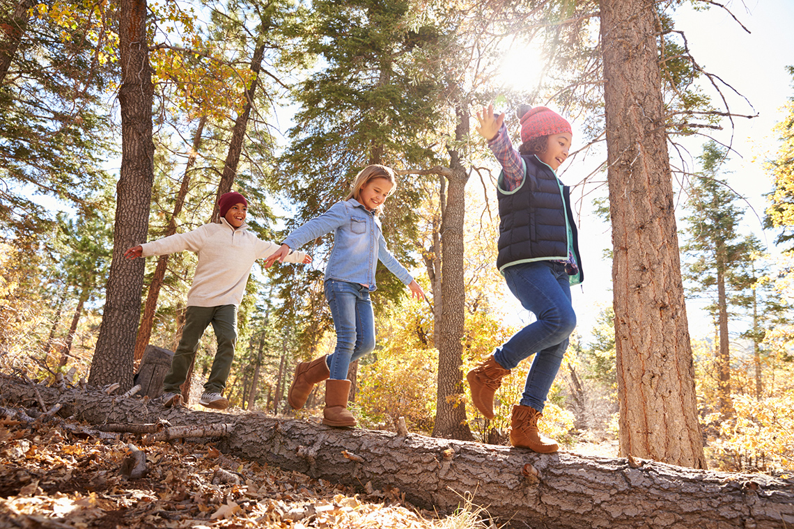 Three children balancing while walking across a log.