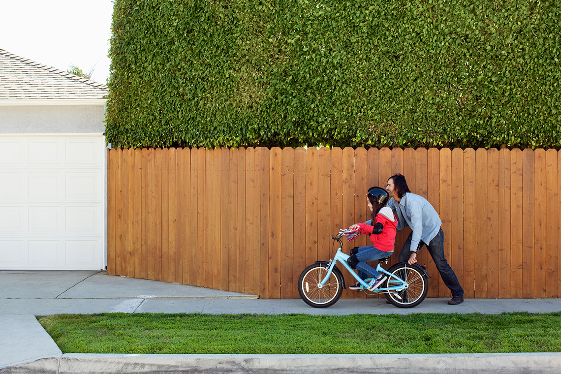 Small child riding their bike with an adult helping them. 