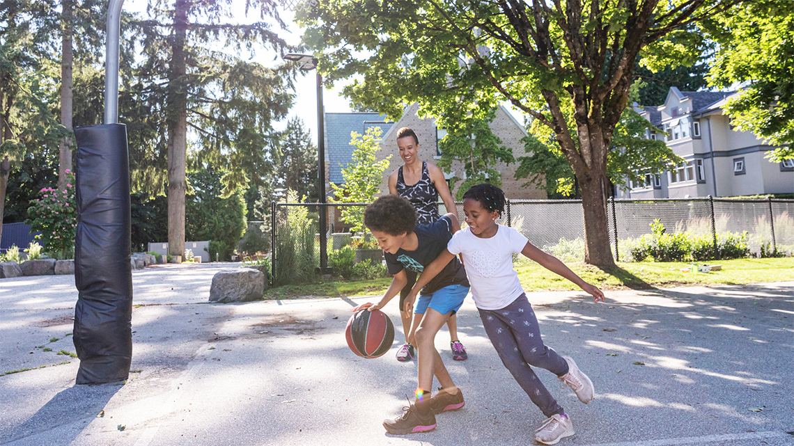 Two children playing basketball outside. One child dribbles the ball while using their other arm to block the other child from stealing the ball.
