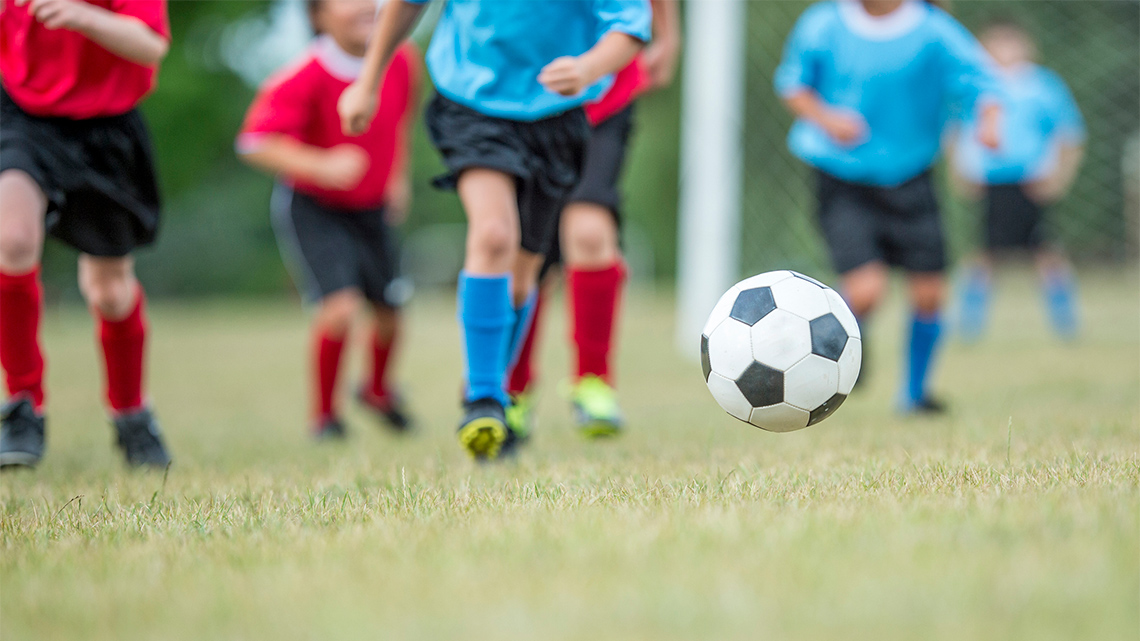 Children in a soccer field chasing after a soccer ball.