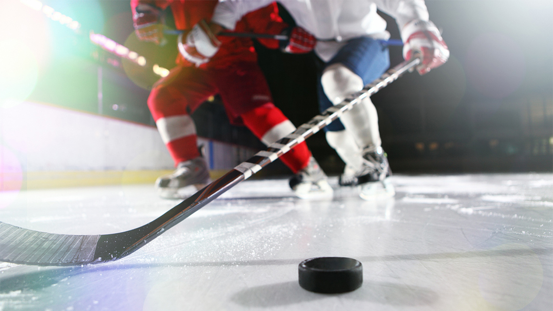 Two hockey players jostling for the hockey puck during an ice hockey game.