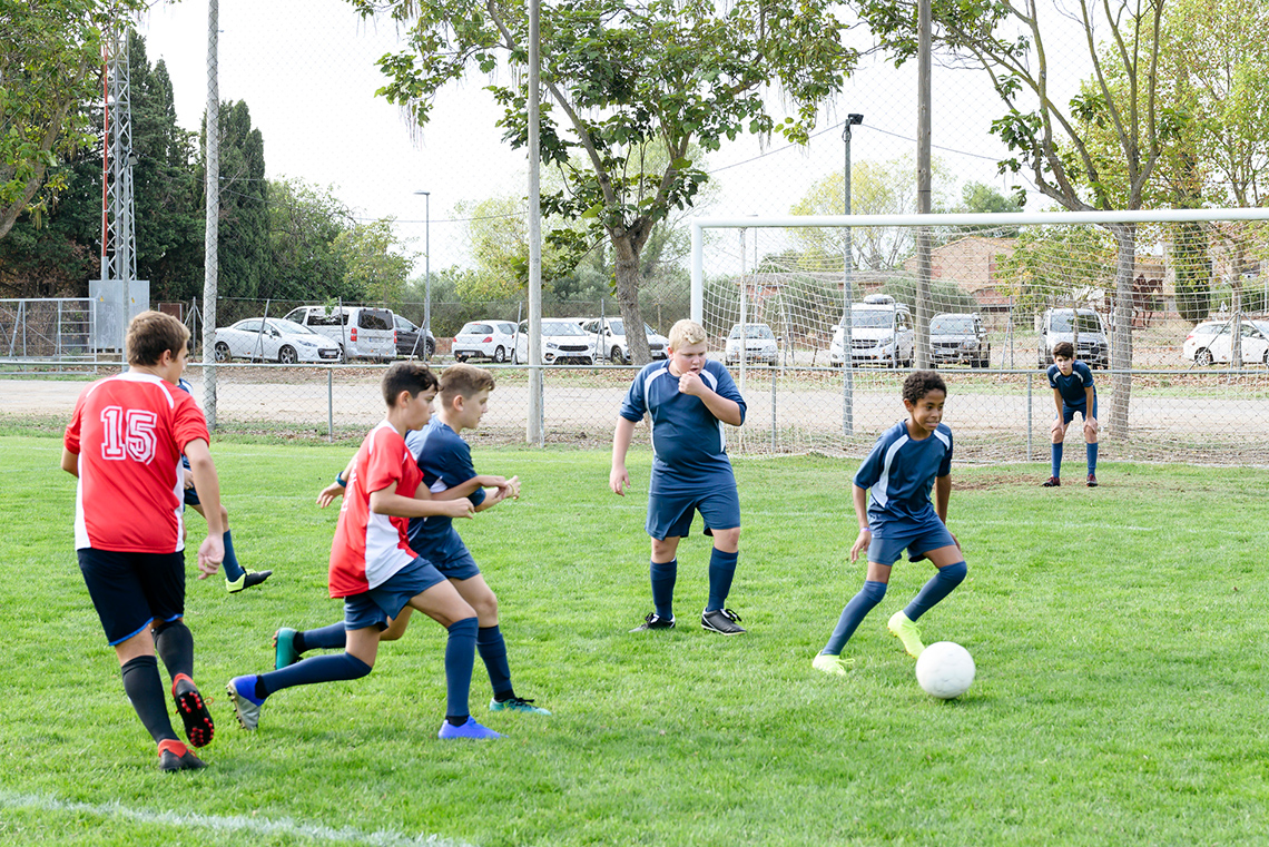 A student dribbling a soccer ball towards a goal post.