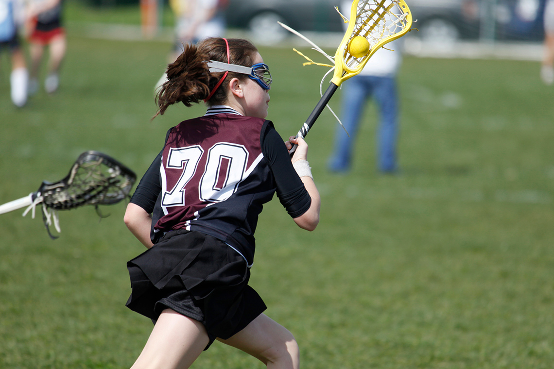 Child keeping ball safe in a scoop while moving across the field.