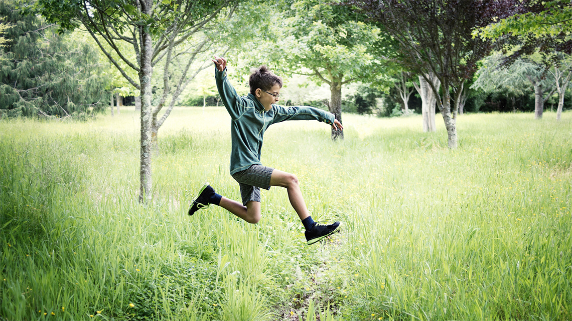 A child is leaping outside. They are taking off on one foot and landing on the other.
