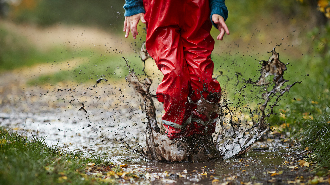 A child hopping into a puddle on the road. They land on two feet in the mud.