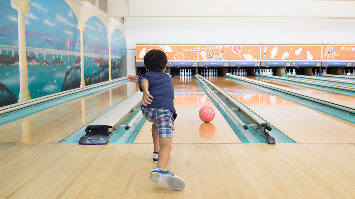 A child rolls a bowling ball down a lane towards bowling pins.