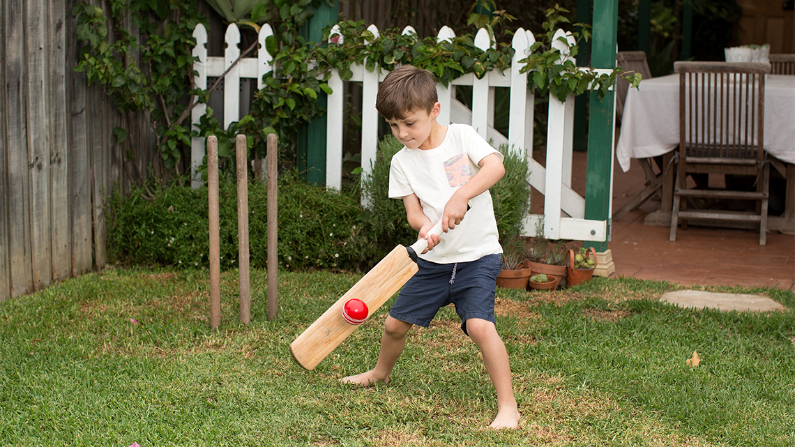 A child swings a cricket bat at a ball.