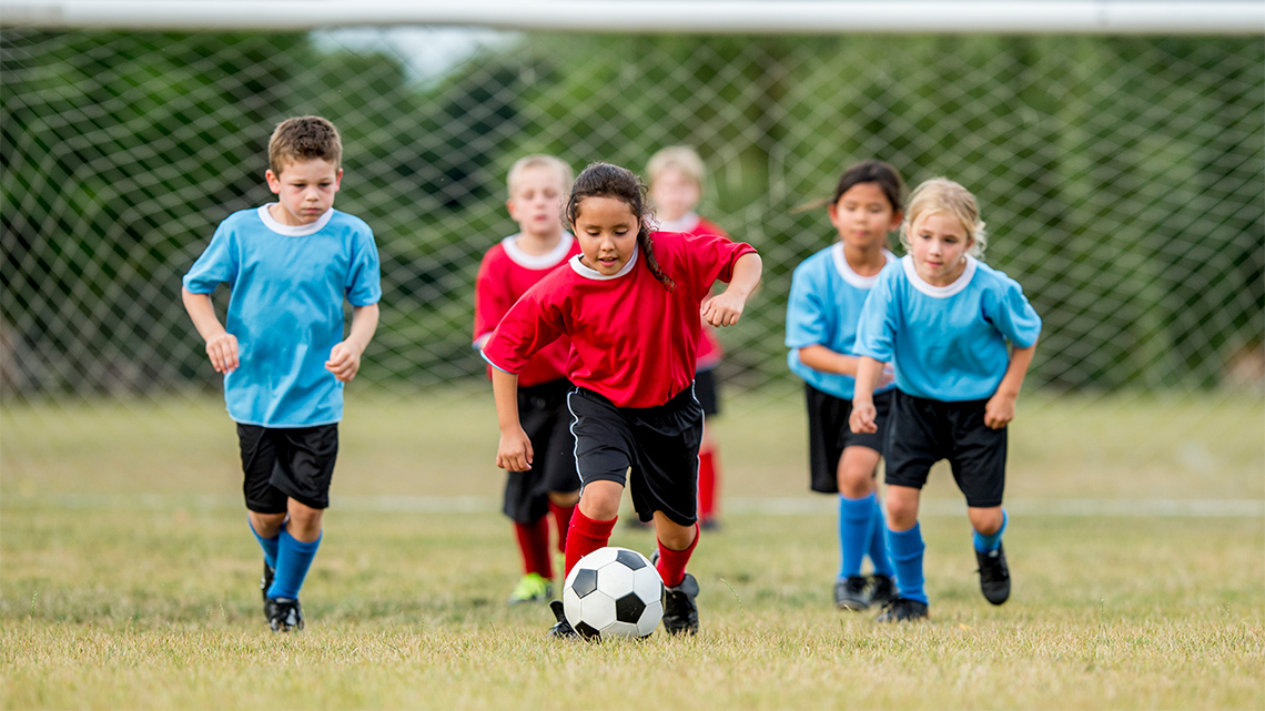 A child dribbles a soccer ball during a soccer game. Children from the other team chase after the child with the ball.