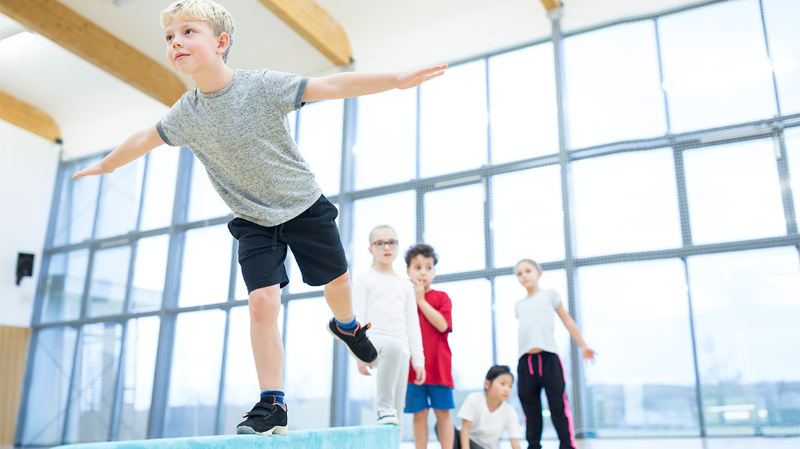 A child balancing on a beam with one foot.