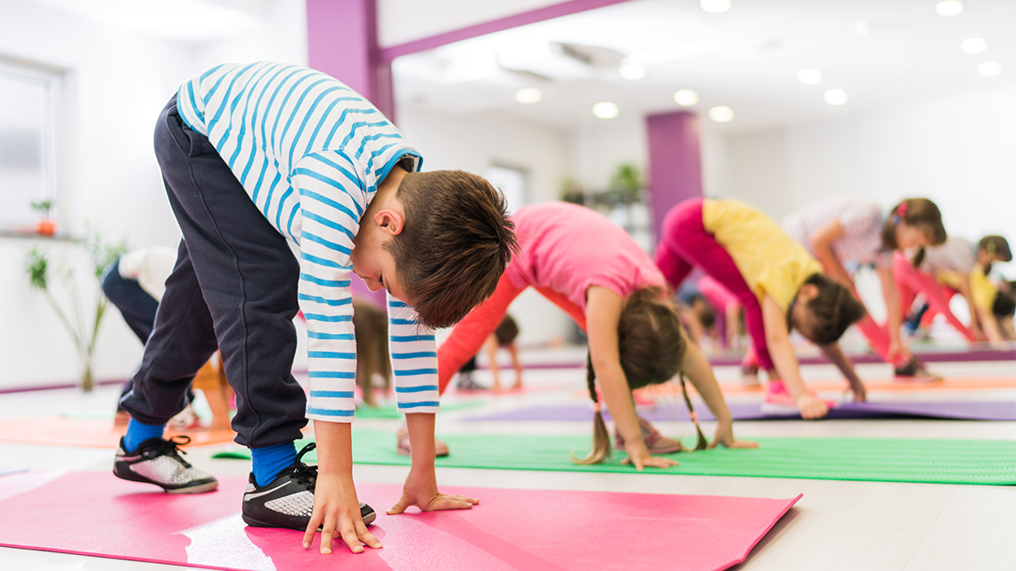 A group of children on mats leaning forward and balancing on two hands and two feet.