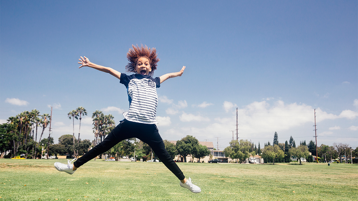 A child jumping with their arms and legs spread apart, making the shape of a star.