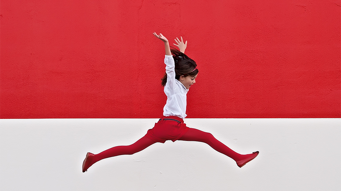 A child jumping with one leg fully extended forward and the other leg fully extended backward.