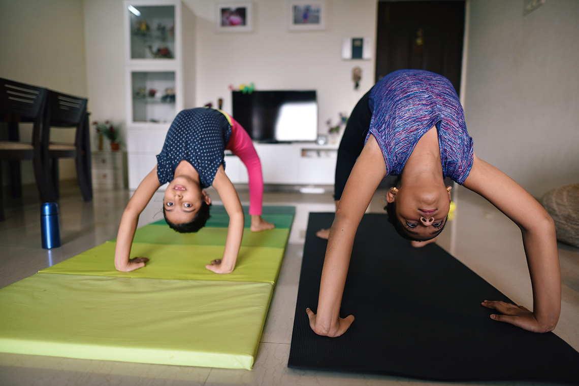 Two children stretching their stomachs upward while balancing upside down on their hands and feet.
