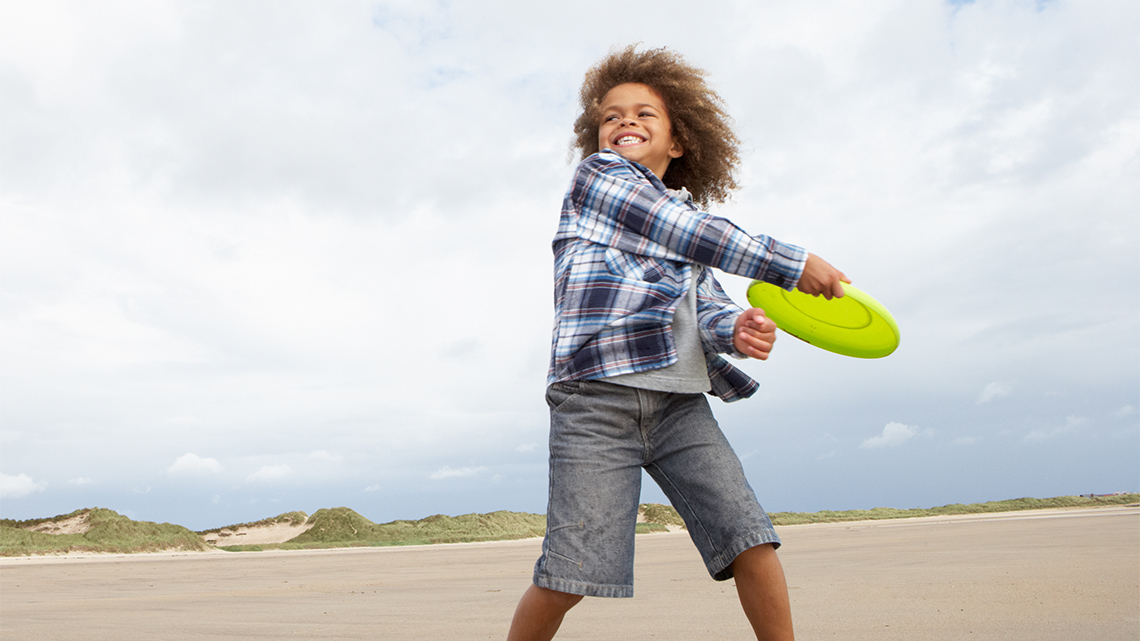 A child holds a flat plastic disc with their arm bent toward their body. 