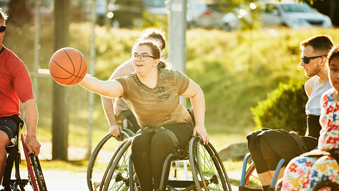 A youth in a wheelchair reaching to grab a ball with one hand.
