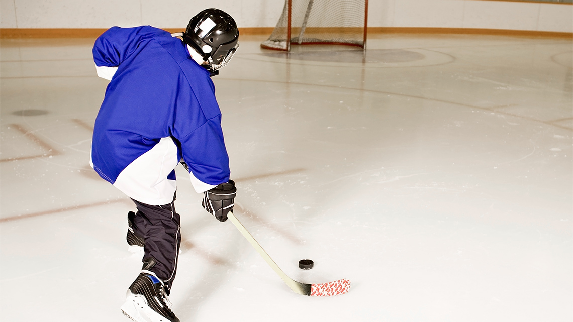 A child swinging a stick to hit a puck into a net.