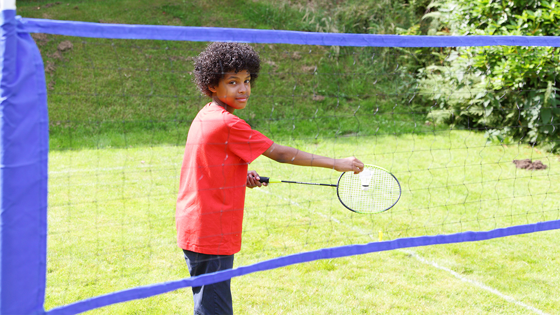 A child holding a birdie to hit with a racquet. 