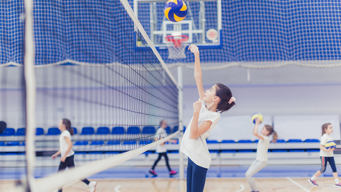 A child hitting a medium sized ball over a net in a gymnasium.