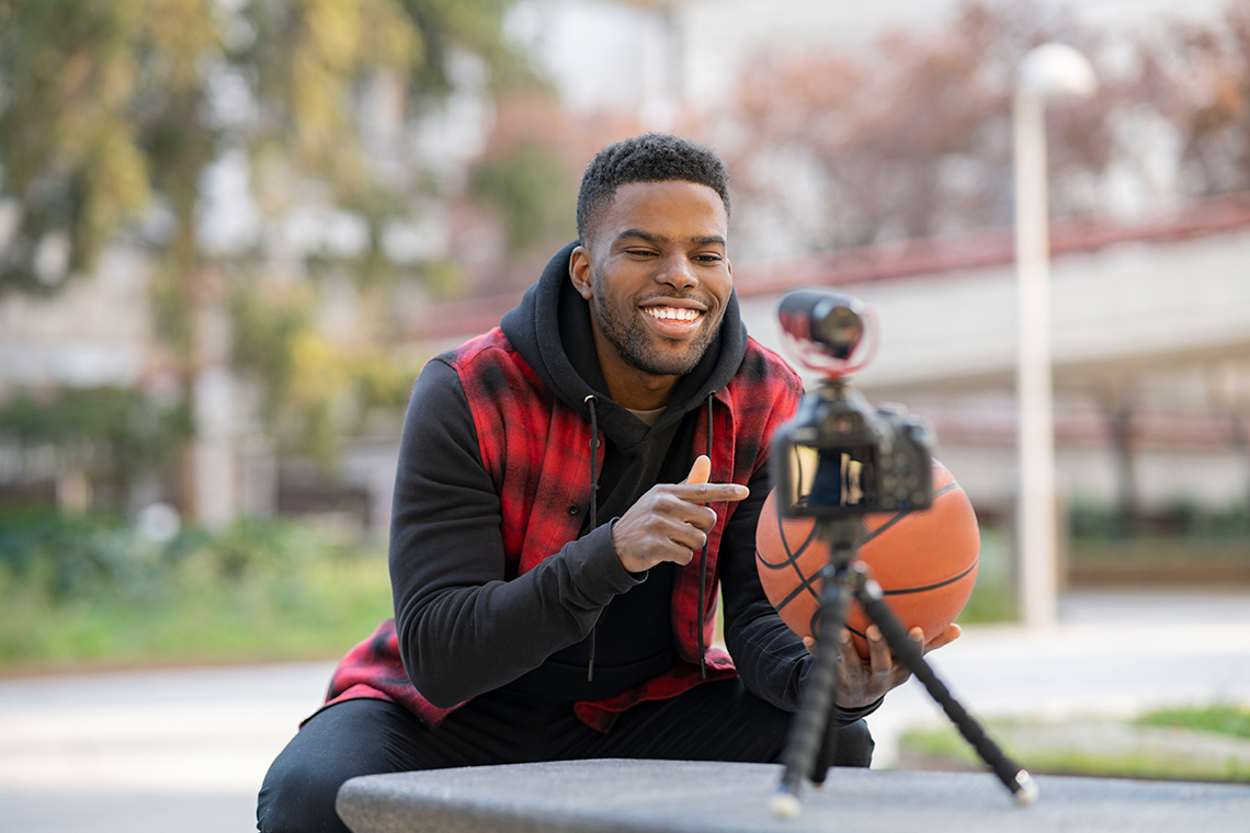 A person holding and pointing at a basketball in front of a video camera that is recording them.