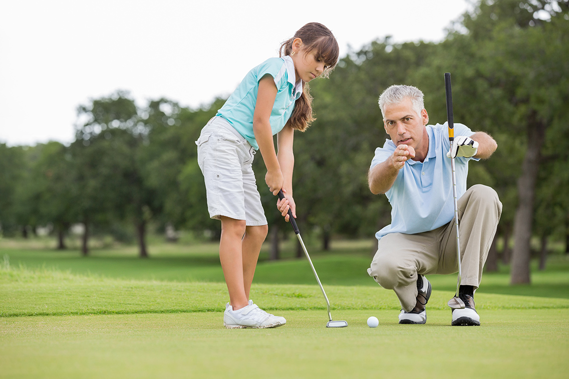 A child setting up their golf club to send a ball into a hole on a golf course.