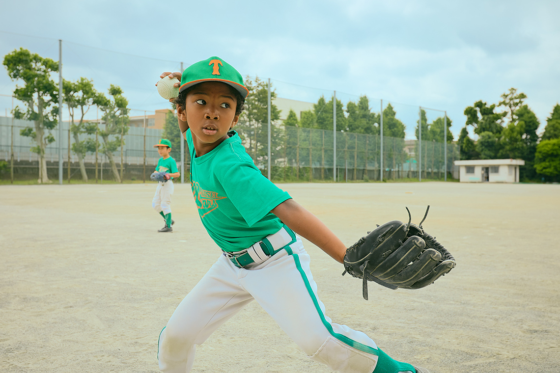 A child wearing a baseball glove preparing to send a ball to teammates.