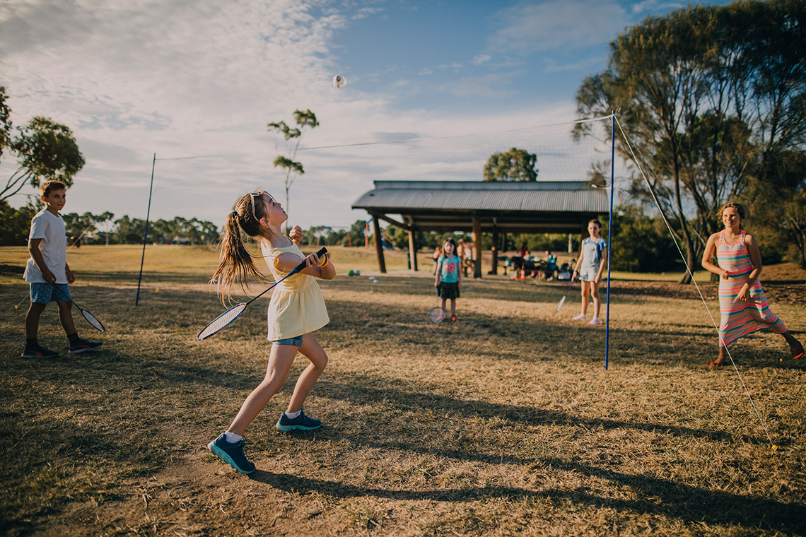A child playing badminton in a park swinging their racquet to send a birdie over the net.