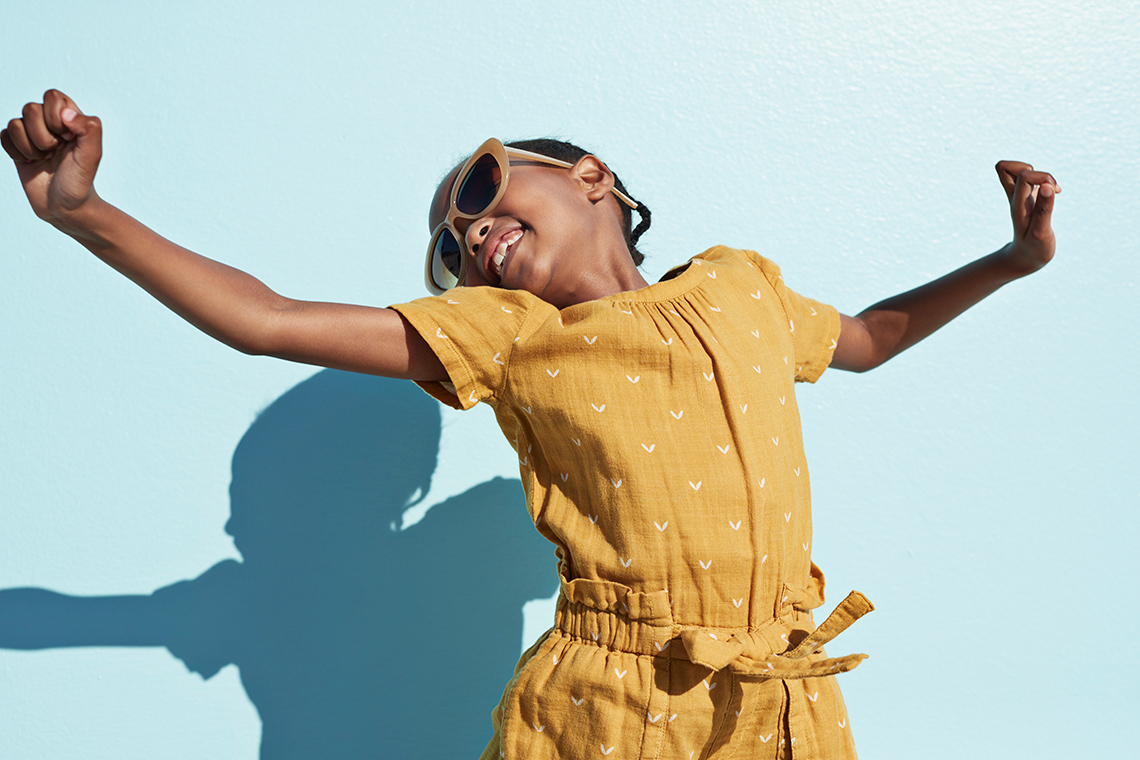 A child dancing on their tiptoes, swinging their arms, and smiling.