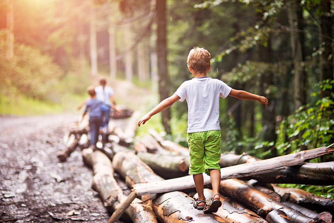 Three people are walking and balancing on a fallen tree trunk.