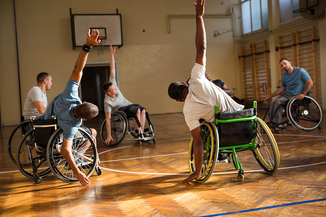 Athletes seated in wheelchairs doing warm-up exercises, with an arm stretched towards the floor and the other arm towards the ceiling.