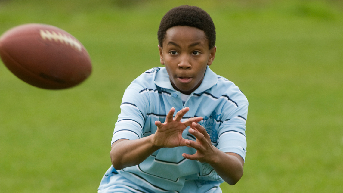 A boy prepares to catch a football by opening his hands in front of his chest.