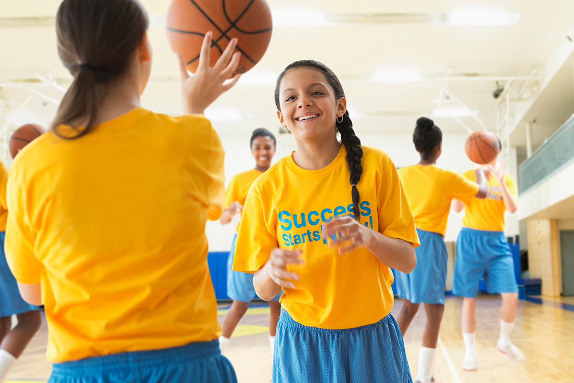 A girl prepares to throw a ball. She holds the ball in front of her and above her shoulders.