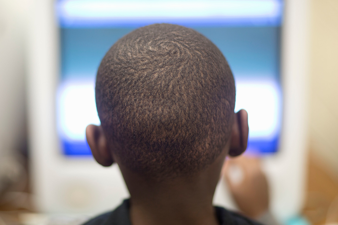 A close-up of the back of a person’s head as they look at a monitor.