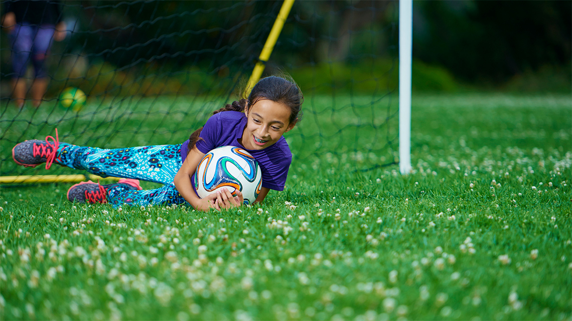 A soccer goalie saves a goal by catching a ball to their chest in mid-air.