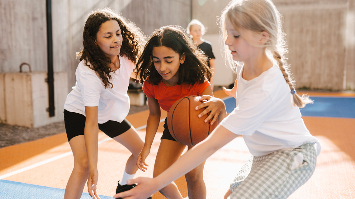 One athlete dribbles a basketball with one hand while a defender blocks the athlete by extending their arms.