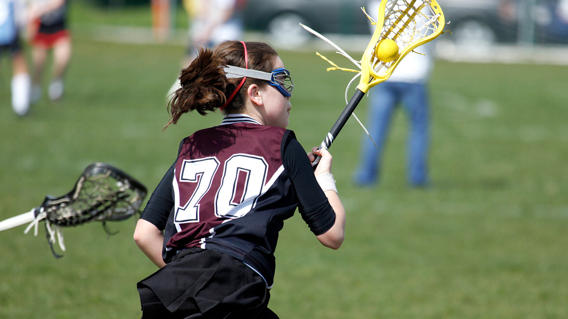 A person is running and carrying a lacrosse ball in their lacrosse stick.